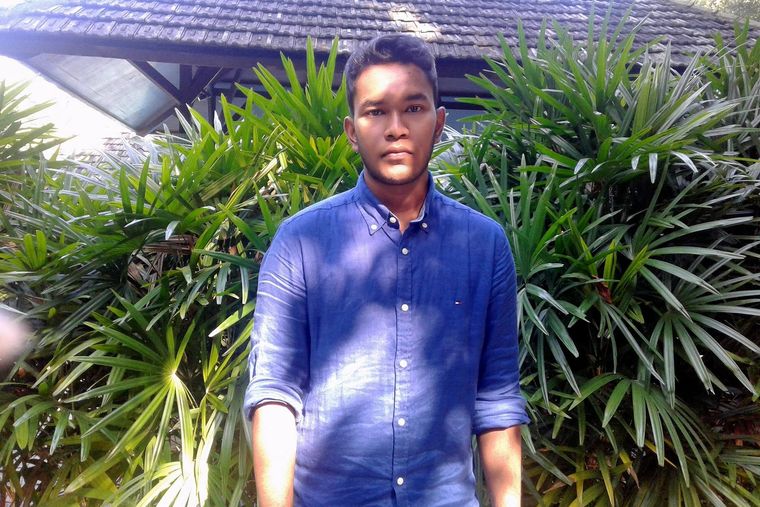 Yusuf in a blue shirt standing in front of tall green palms at a garden resort.