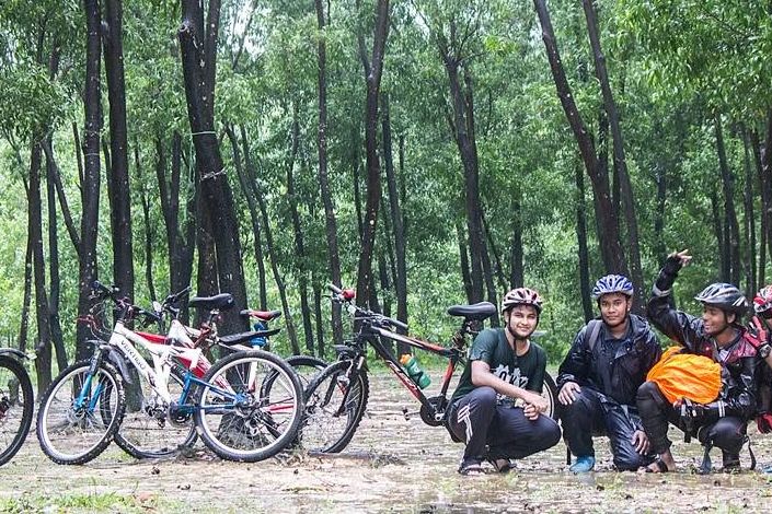 Yusuf crouching with three friends beside their mountain bikes in a wet forest clearing after a ride in the rain.